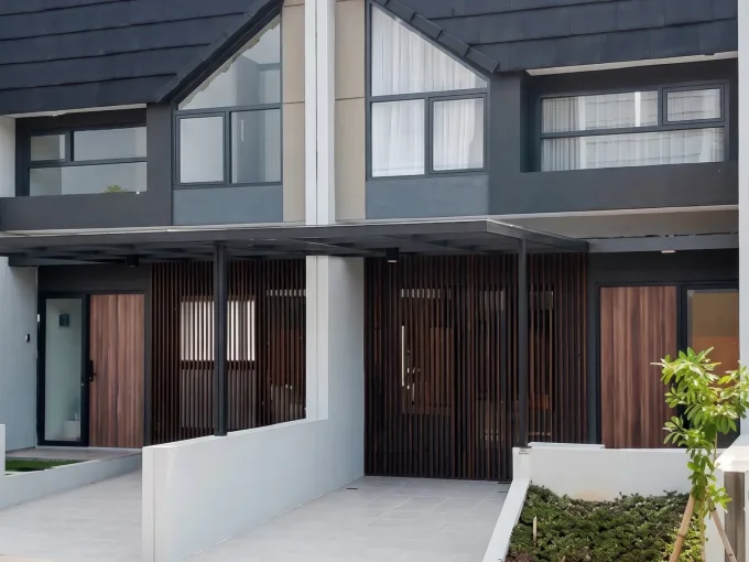 Front view of a modern two-unit townhouse with dark gray siding, sloped roofs, and large rectangular windows overlooking a paved entrance.