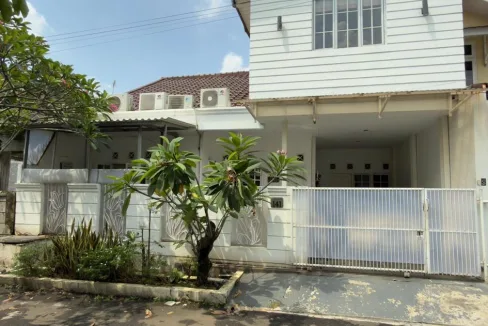 White Twostory House with a White Metal Gate a Small Front Garden with a Flowering Tree and Several Air Conditioning Units on the Roof Against a Blue Sky  Rooma21com