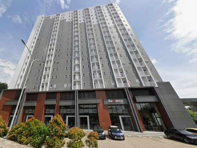 Tall grey and white high-rise residential building with a red-brick ground floor and glass entrances, cars parked out front.